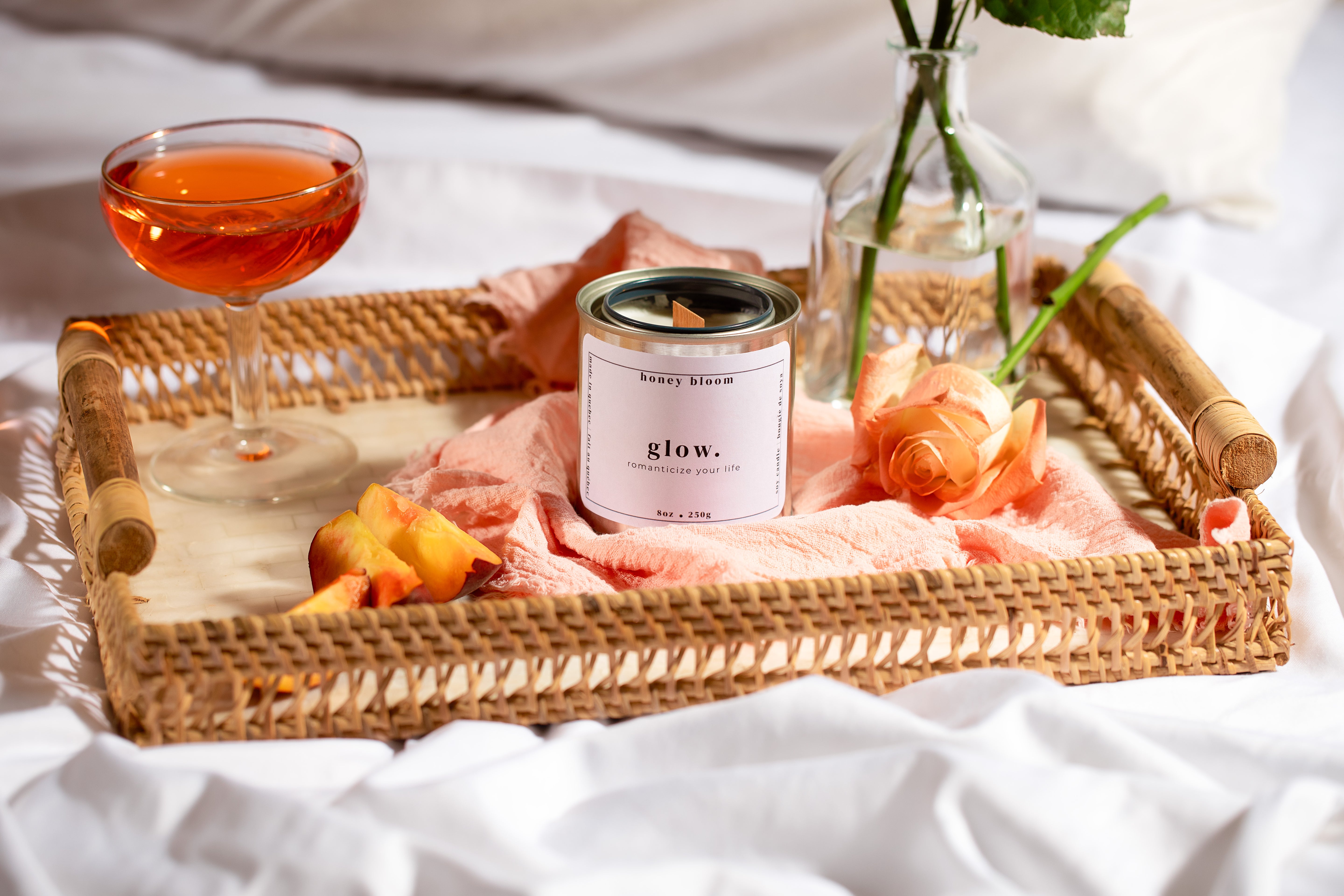 Artisanal hand-poured soy candle from a Québec candle brand, photographed in a romantic slow-living scene with roses, a drink, and sun-lit textures.