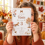 A young girl with curly hair holds a fall-themed 3rd birthday invitation card in front of her face. The card features autumn illustrations including a fox, tree, pumpkin, and leaves, with the text 'Rosie is turning 3'.