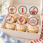 Six cupcakes in an ivory bakery box with vintage circus toppers featuring an elephant, tent, carousel horse, balloons, and birthday designs.