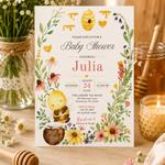 Honey bee baby shower invitation standing on a wooden table beside daisies, a honey jar and a glowing candle.