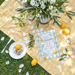 Overhead flat lay of a lemon-themed 21st birthday party invitation with daisies, lemons and yellow gingham