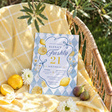 Freshly 21 birthday invitation displayed on a wicker chair with lemons, figs, flowers and yellow gingham fabric