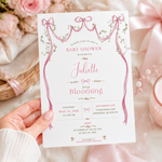 Hand holding a baby shower invitation featuring pink watercolor ribbon bows, delicate flowers and personalized text.