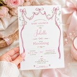 Hand holding a baby shower invitation featuring pink watercolor ribbon bows, delicate flowers and personalized text.