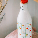 White bottle with red cap and fruit pattern on a light surface