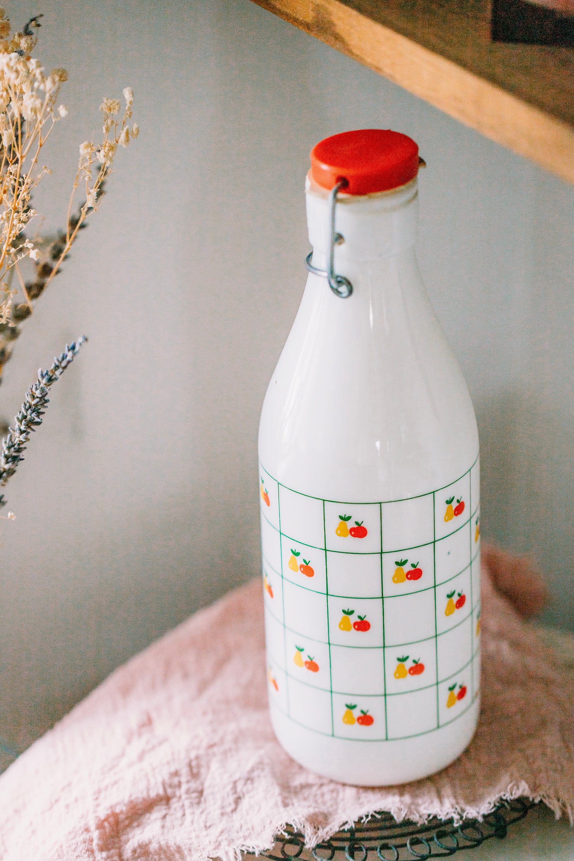 White bottle with red cap and fruit pattern on a light surface