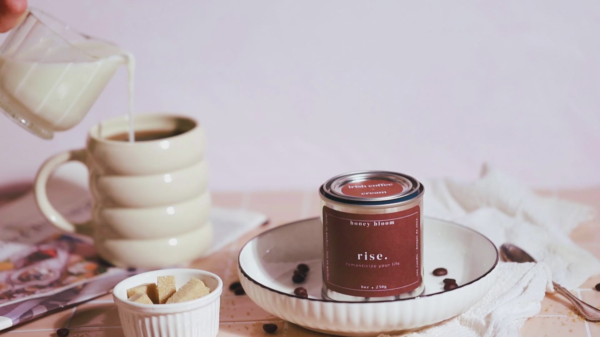 Short video showing a hand-poured soy candle from a Québec artisanal candle brand, filmed in a soft morning coffee ritual with cream being poured, brown sugar, and warm pastel styling.
