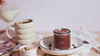 Short video showing a hand-poured soy candle from a Québec artisanal candle brand, filmed in a soft morning coffee ritual with cream being poured, brown sugar, and warm pastel styling.