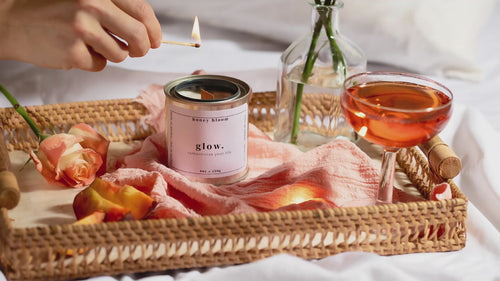 Video of the handmade soy candle “Glow” by Honey Bloom, an artisanal Québec candle brand, being lit in a romantic slow-living scene with roses, a cocktail glass, and warm natural light.