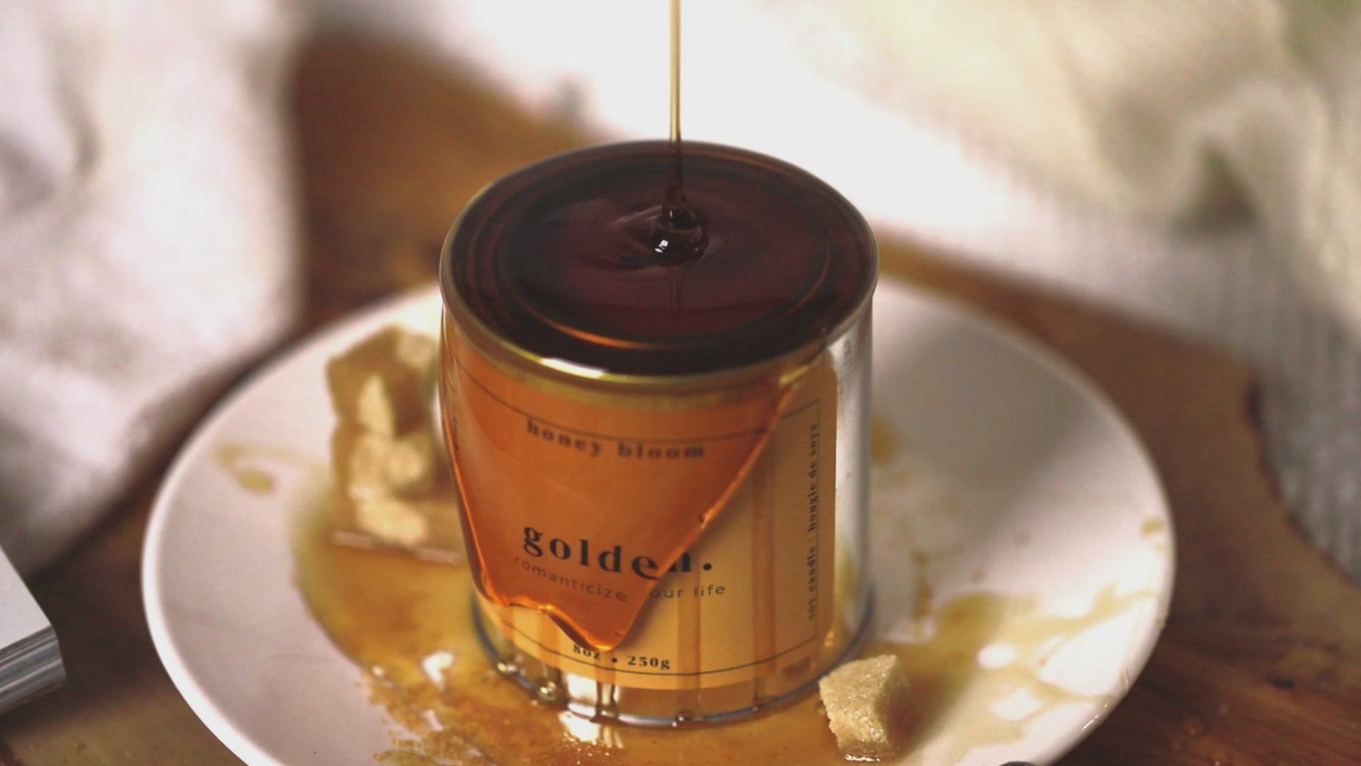 Video showing honey slowly pouring over the handmade soy candle “Golden” from a Québec artisanal candle brand, styled with sugar cubes and warm natural light.