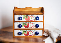Vintage ceramic drawer organizer with apple motif and blue knobs on wooden table