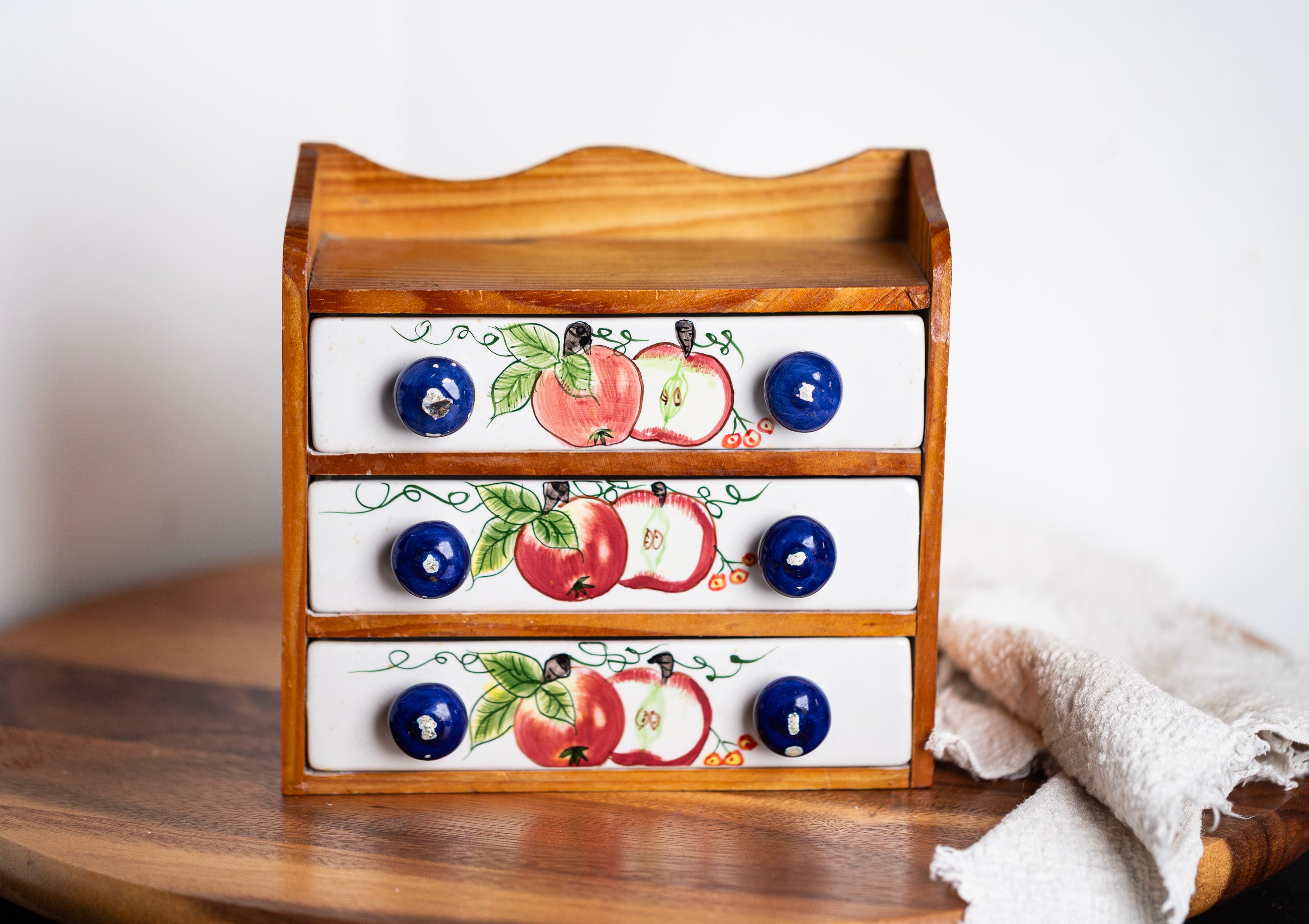 Vintage ceramic drawer organizer with apple motif and blue knobs on wooden table