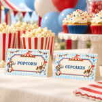 Vintage circus popcorn and cupcake food tent cards on a party table with striped popcorn boxes and frosted cupcakes.