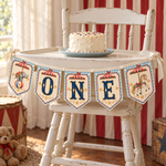 Vintage circus ONE banner hanging across a white high chair with a birthday cake and red striped backdrop.