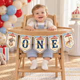 Smiling baby in a wooden high chair decorated with a vintage circus ONE banner, elephant and carousel horse pennants.