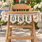 Five-piece vintage circus ONE banner on a wooden high chair outdoors, surrounded by greenery.