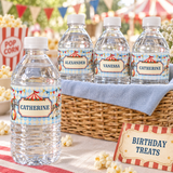 Personalized circus water bottles displayed in a wicker basket with blue linen at a birthday party favor station.