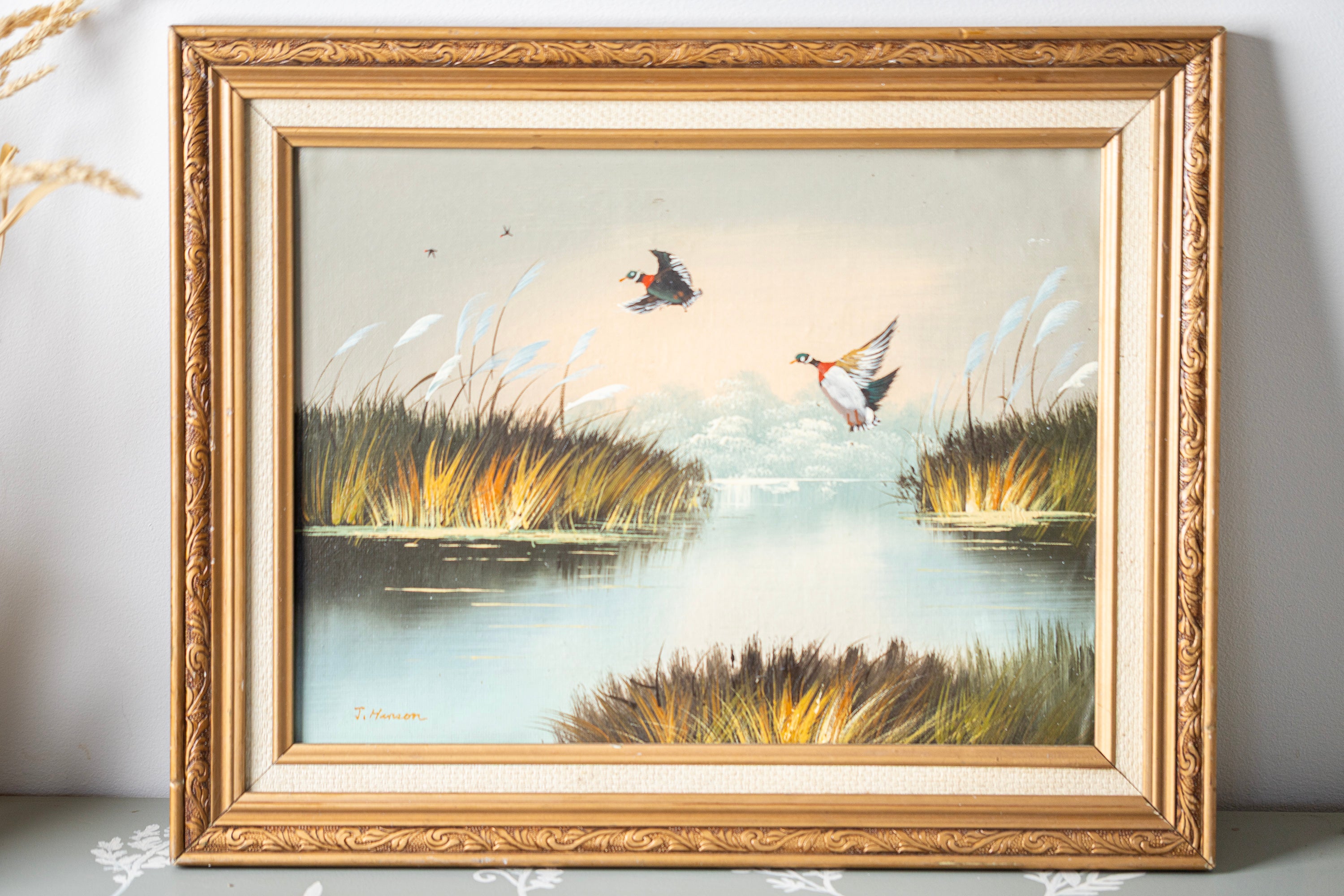 Framed painting of ducks in a marshy landscape with reeds and water.