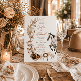 A rustic wedding invitation card featuring watercolor floral illustrations, a horse, and cowboy hat motifs, styled on a wooden table with plates, a candle, dried flowers, and a hat in a warm, decorated event setting.