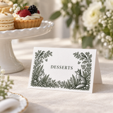 Folded woodland wedding food tent labeled Desserts, with green botanical, rabbit and fox illustrations beside a pastry stand.